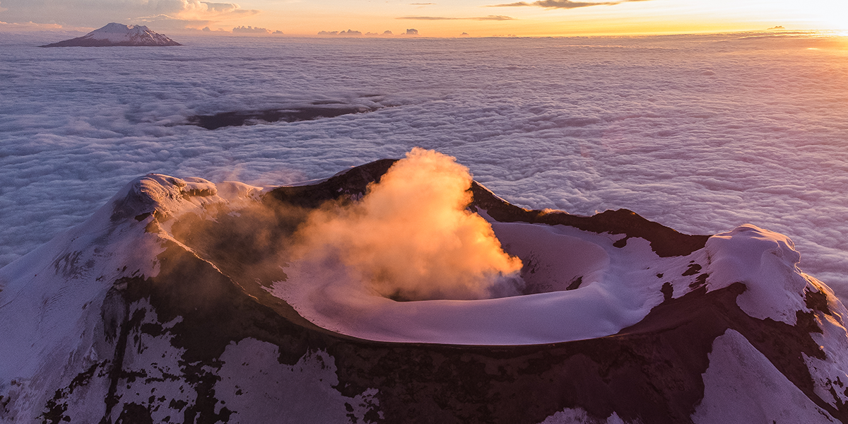 Montañistas en la cumbre del Cotopaxi al amanecer con un mar de nubes debajo.