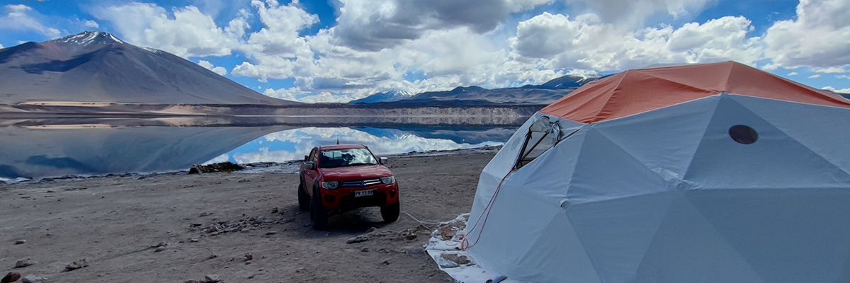 Un vehículo 4x4 de HME a orillas de la Laguna Verde, con las aguas turquesas y el volcán Ojos del Salado nevado al fondo.
