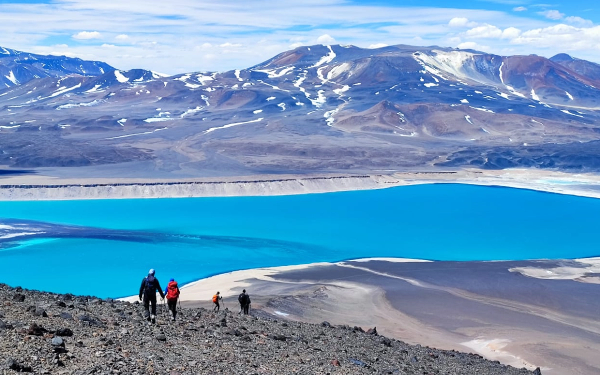 Mountaineers hiking Mulas Muertas peak with a scenic view of Laguna Verde during Ojos del Salado 14-day expedition.